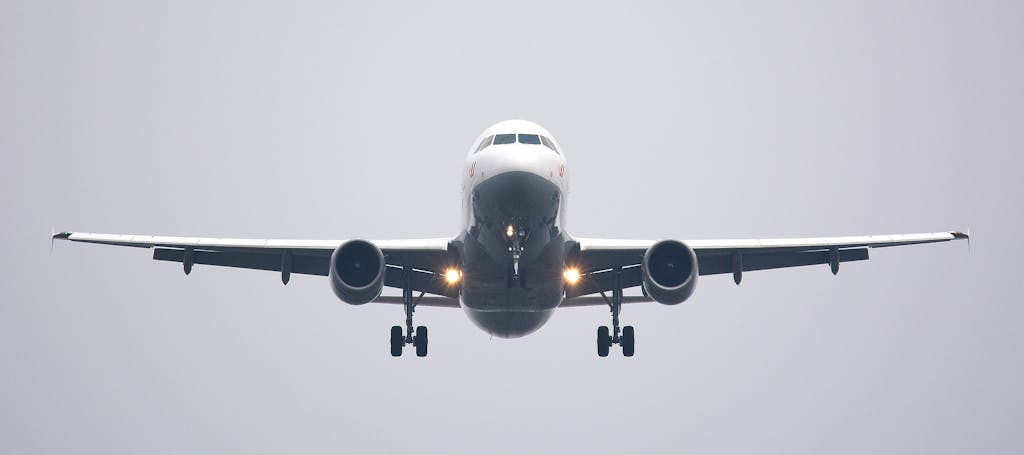 A commercial airliner captured head-on, preparing to land against a cloudy sky.