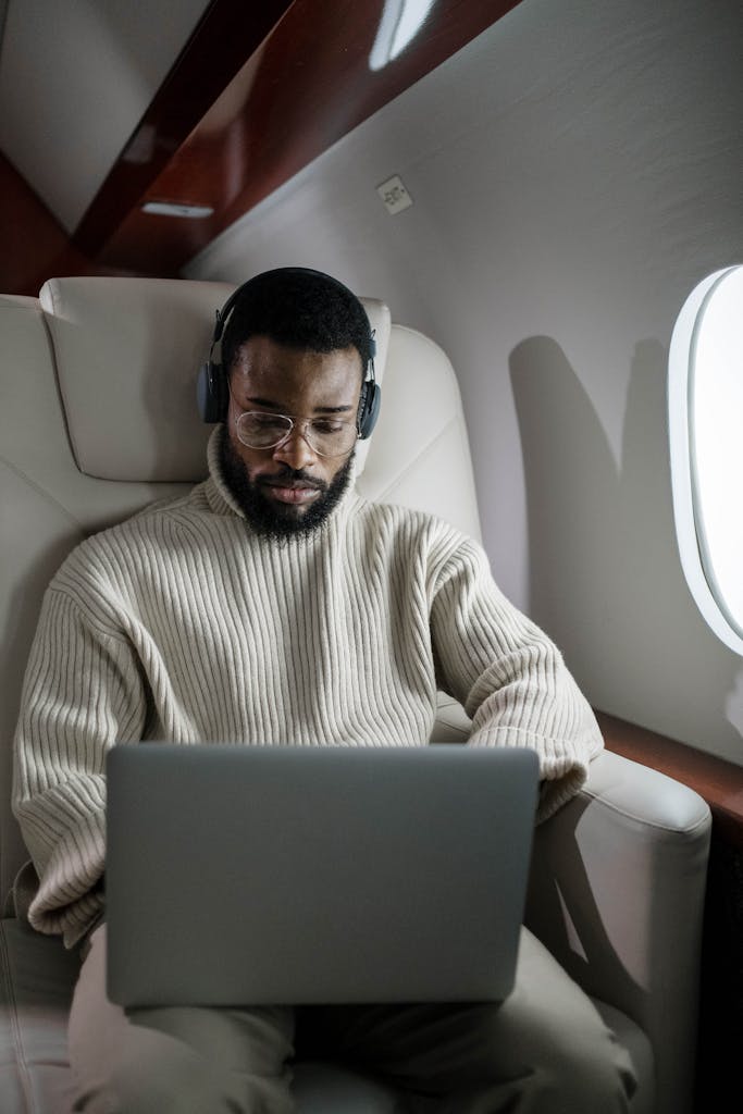 A focused businessman using a laptop and headphones while traveling on a private jet.