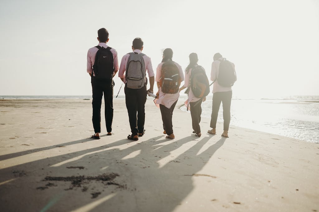A group of friends with backpacks enjoys a sunny day walking along the beach shoreline.