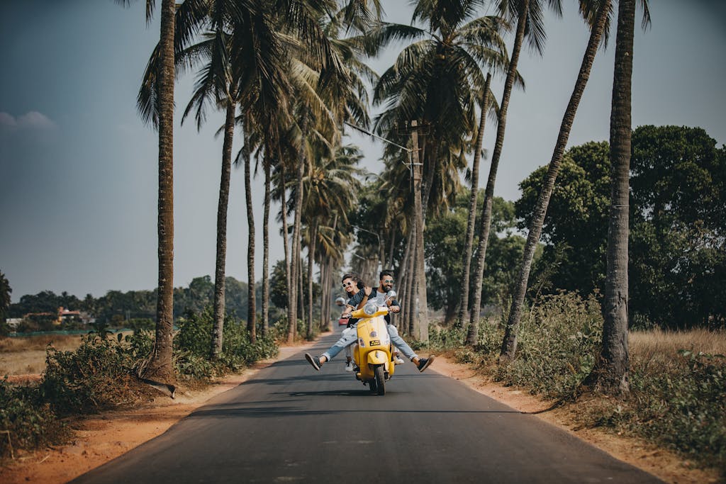 A joyful couple rides a yellow scooter through a scenic palm-lined road, capturing the essence of tropical travel and adventure.