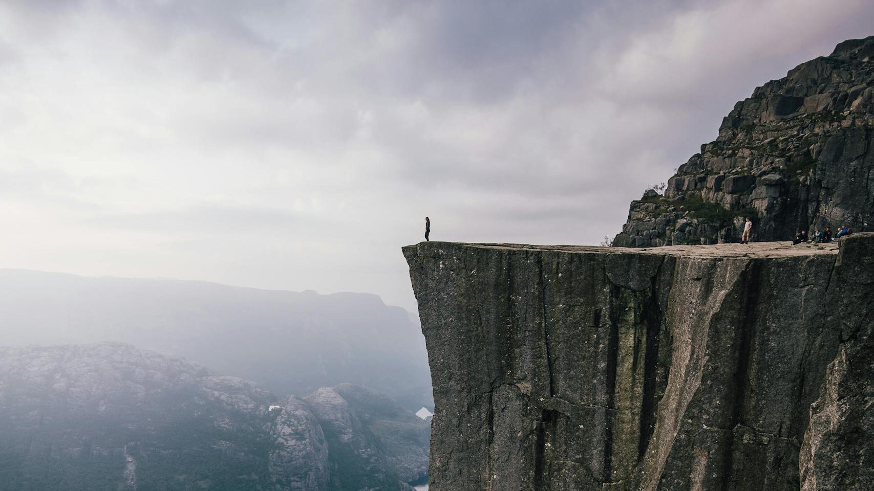 A lone adventurer stands on the edge of Preikestolen cliff, overlooking the stunning fjord below in Norway.