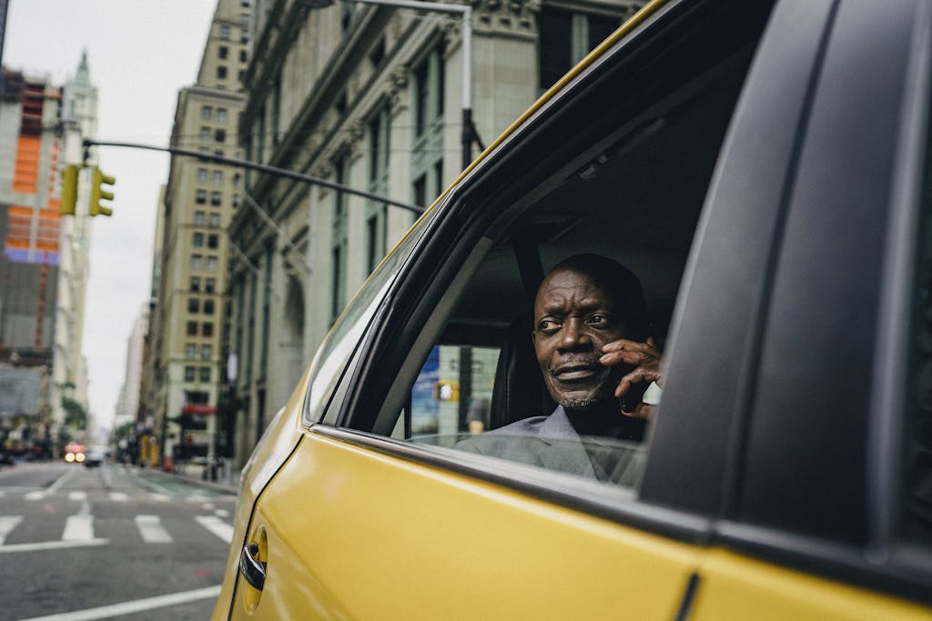 A man converses on the phone in a yellow taxi, set against the vibrant streets of New York City.