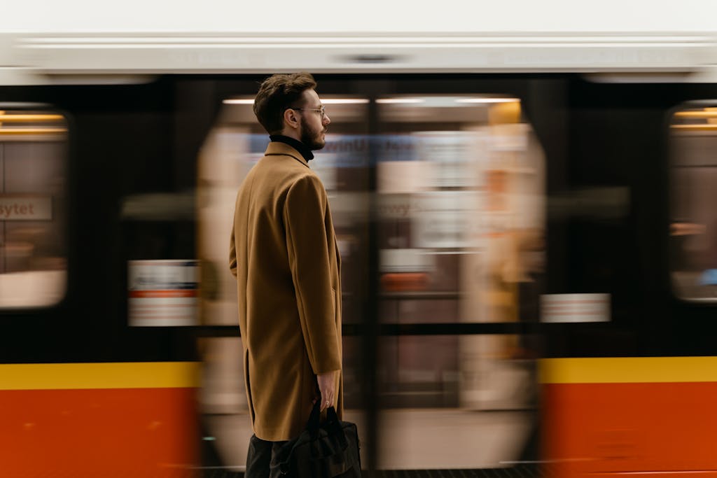 A man with a beard stands in focus against a moving train background at a station.