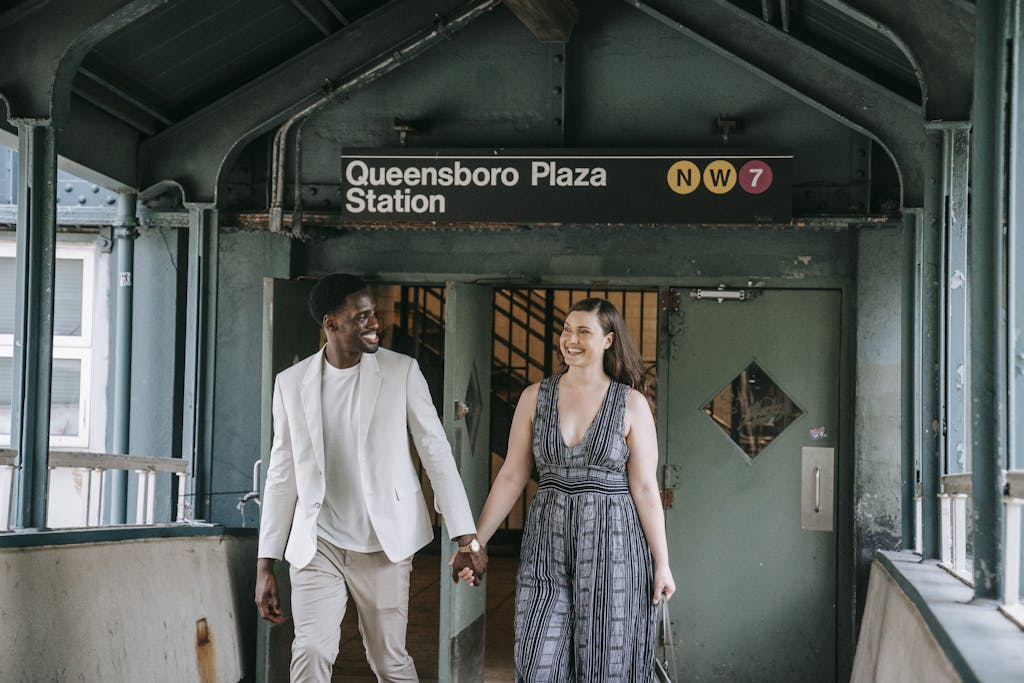 A smiling couple holding hands at Queensboro Plaza Station in New York City.