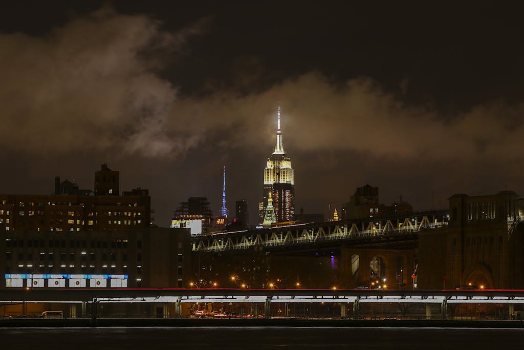 Captivating night view of the Empire State Building illuminated above the Brooklyn Bridge in New York City.