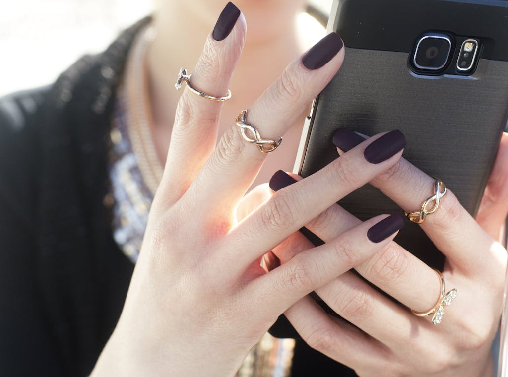 Close-up of a woman with manicured nails and rings holding a smartphone, showcasing fashion elegance.