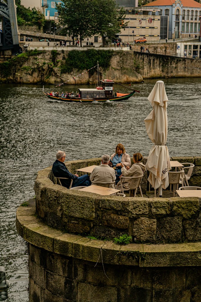 Group of adults sitting by the Douro River in Porto, Portugal, with a boat in the background.