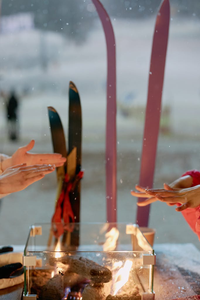 Hands warming by a fire with skis in the background on a snowy winter day. Perfect winter retreat scene.