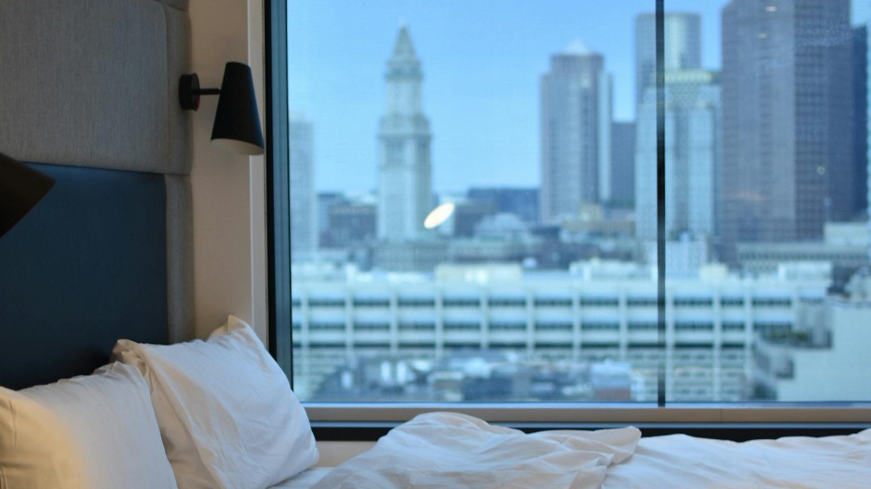Modern hotel room overlooking Boston skyline, featuring luxury bedding.