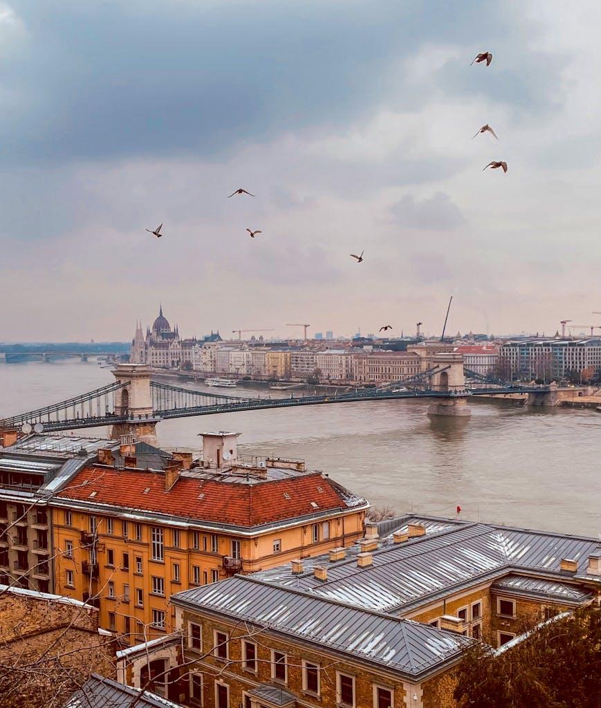 Picturesque Budapest skyline featuring the Chain Bridge and Danube River under a cloudy sky.