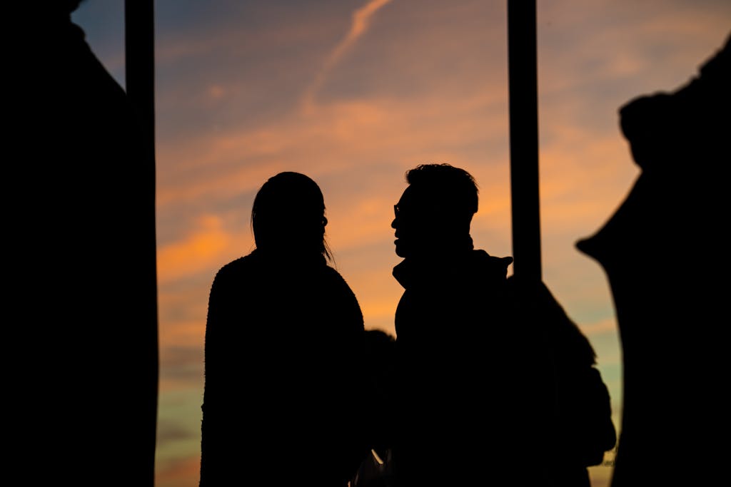 Silhouettes of two people engaged in conversation during a vibrant sunset.