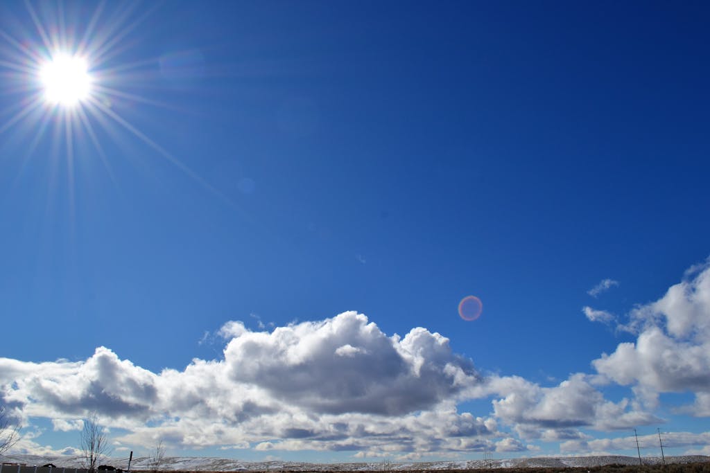 A vibrant image capturing the sun shining over fluffy clouds in a blue sky.
