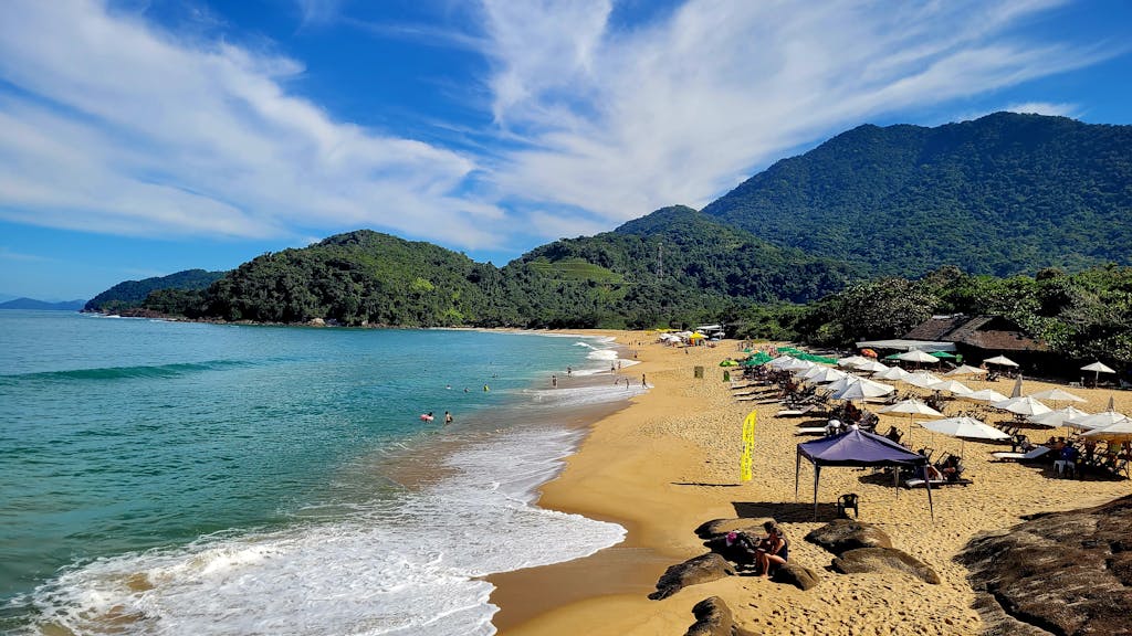Explore the serene sandy shores of Ubatuba, Brazil, with lush mountains and turquoise waters.