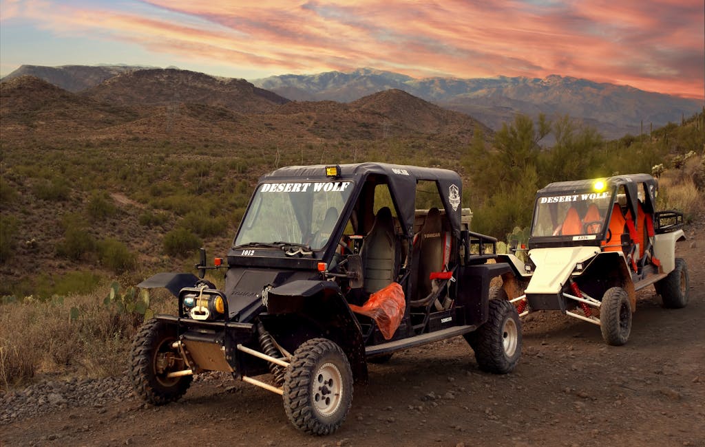 Explore the stunning Scottsdale desert landscape with rugged off-road vehicles on a dirt trail at sunset.