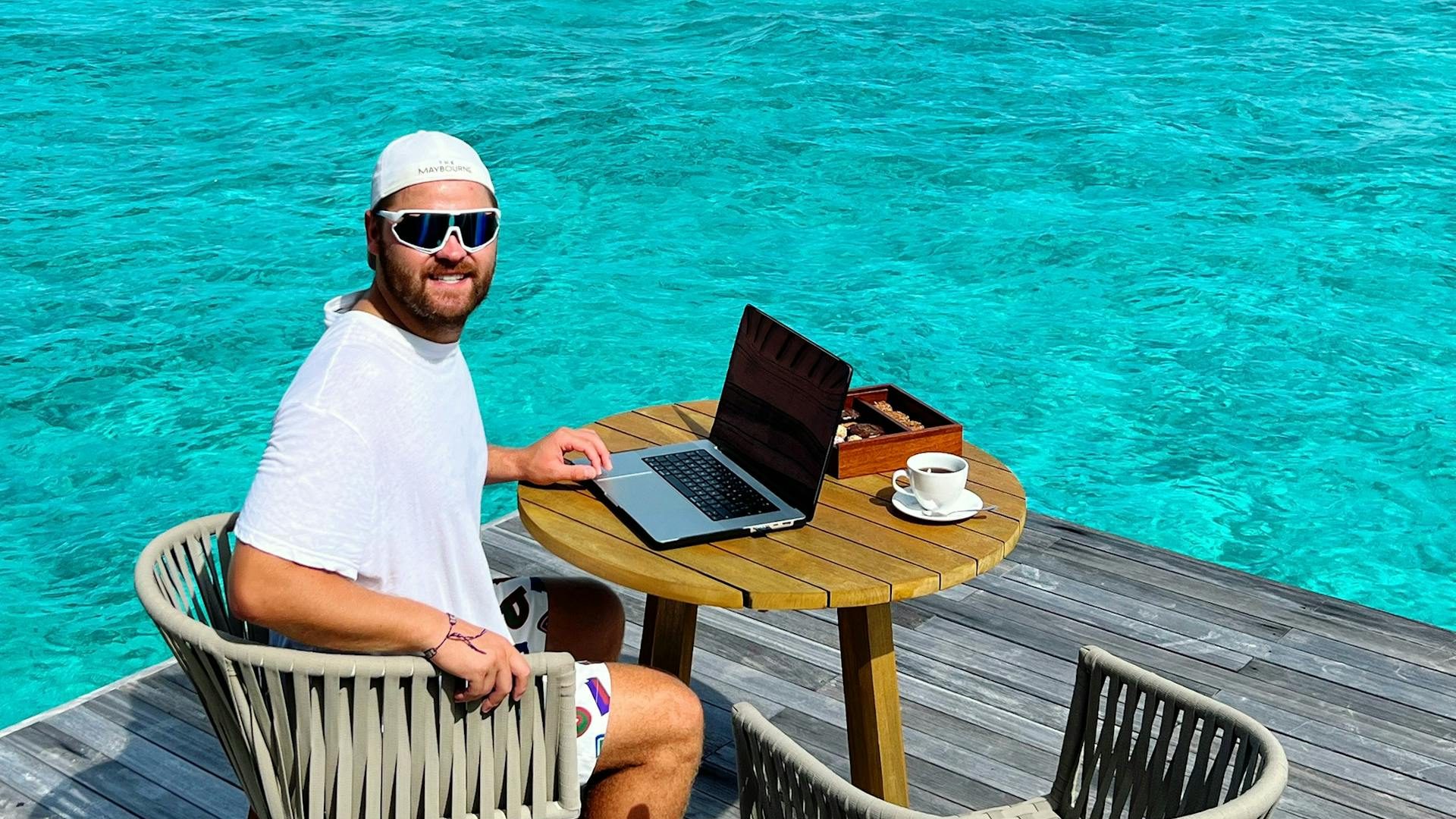 Man working on a laptop by the ocean, embodying remote work lifestyle.