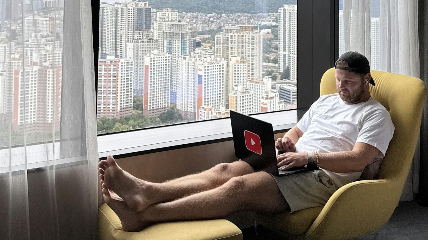 Man working on a laptop in a hotel room with a view of Seoul's skyline and Namsan Tower.