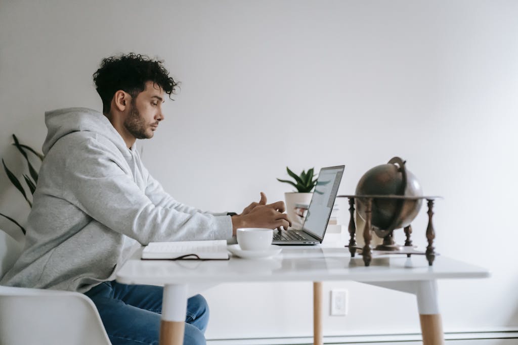 Man working on laptop at home office table with coffee and globe decor.