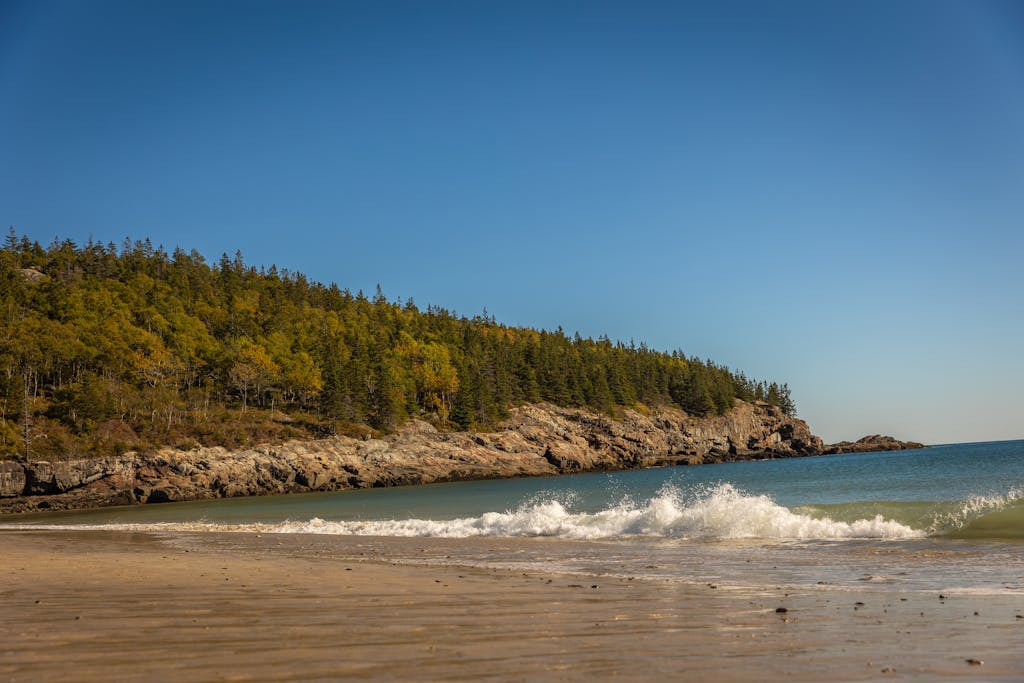 Waves crashing on a sandy beach with rugged cliffs in Acadia National Park.